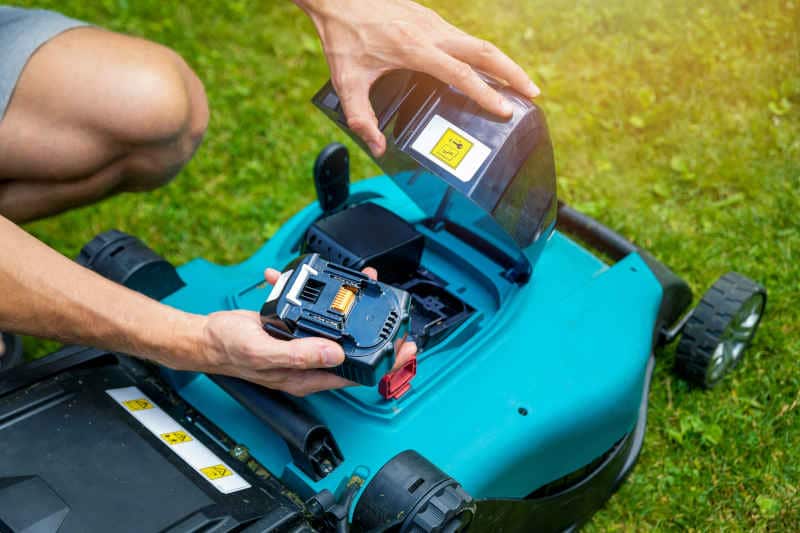 Gardener putting battery into electric cordless lawn mower