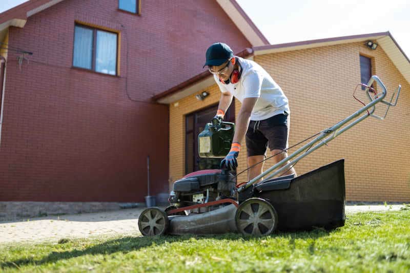 Gardener with a can of gasoline in his hands unscrews the fuel cap of a lawn mower