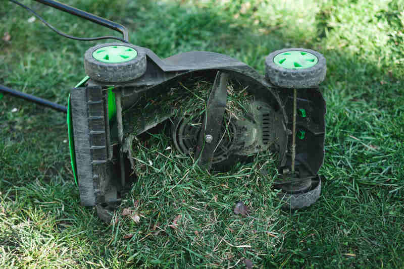 Lawn mower overflowing with grass lies on its side